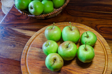 Green apples on a wooden cutting board sitting on a wooden table
