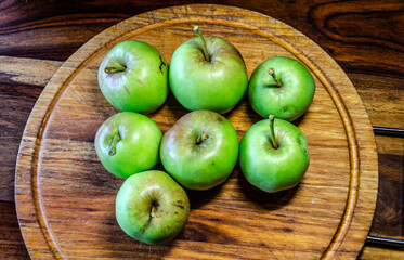 Green apples on a wooden cutting board sitting on a wooden table