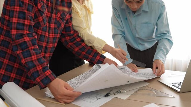 Professional engineer team discussion about house design on meeting table with architectural equipment and building blueprint scatter around at modern office. Focus on hand. Closeup. Delineation.
