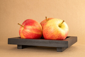Three red apples on a wooden black tray on kraft paper, macro.