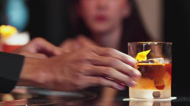 Closeup hand bartender serving Old fashioned cocktail with orange peel on top of rock ice to VIP guest with couple for making special drink advertisement alcohol at nightlife luxurious bar. Vinosity.