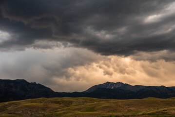 Dark, heavy clouds hover over a range of hills and distant mountains.
