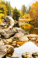 Autumn trees reflect in a river with rocks, a power tower, and forest