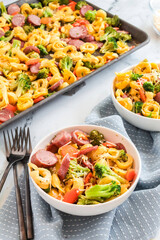 Bowls of tortellini with sausage and veggies next to sheet pan