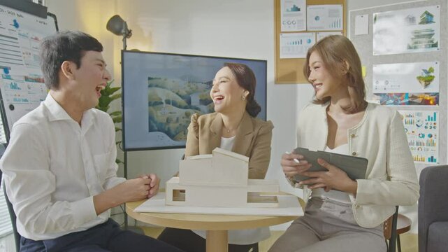 Diverse team of architects and professionals discussing house model in office meeting. The participants are engaged in an in-depth conversation, with architectural drawings displayed in the background