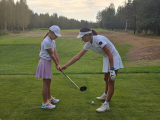 Young girl receives golf instruction on a course in a serene wooded landscape during late