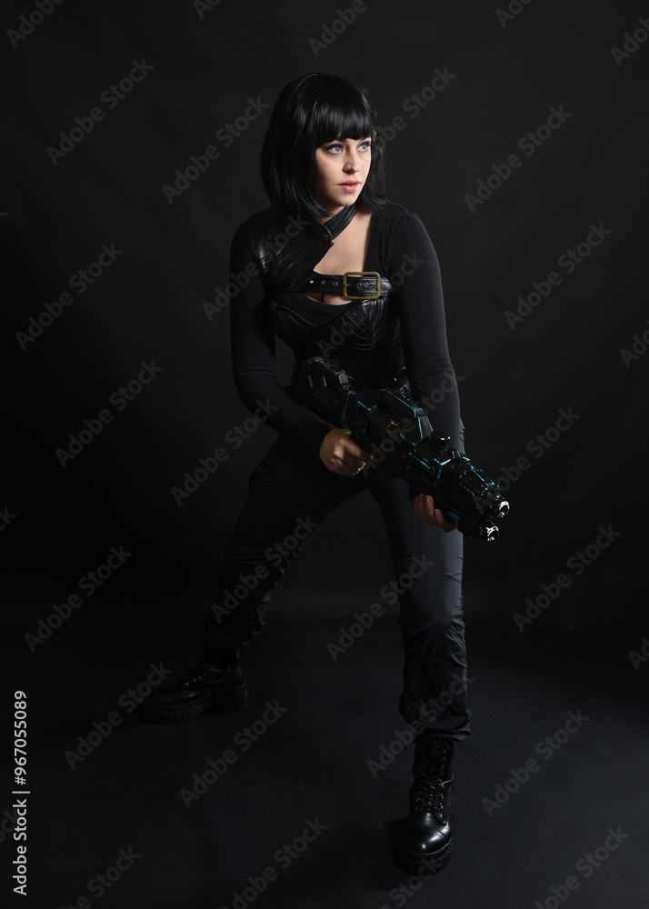 Sticker Full length portrait of beautiful black female model wearing sci fi futuristic dystopian leather bodysuit costume. Standing pose, holding gun weapon. isolated dark studio background moody silhouette.