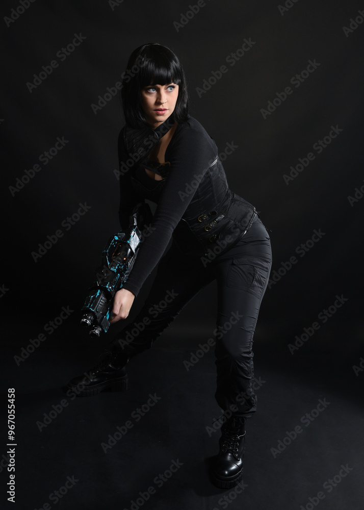 Canvas Prints Full length portrait of beautiful black female model wearing sci fi futuristic dystopian leather bodysuit costume. Standing pose, holding gun weapon. isolated dark studio background moody silhouette.