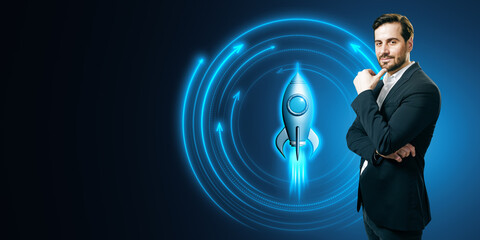Attractive smiling young european businessman with glowing rocket on blue background with mock up place. Digital transformation, start up and boost concept.