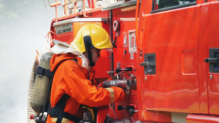 Naklejka premium Fireman prepare equipment fighting extinguisher at fire engine truck. Firefighter fighting with smoke flame using fire hose, tube, chemical water foam spray at truck. Fireman wear hard hat protection