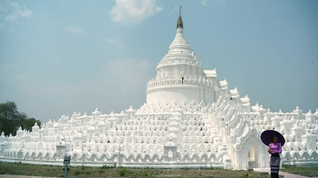 Pretty woman in treaditional suite holding violet paper umbrella travel and make a merit at Hsinbyume Pagoda in Mingun Mandaley, Myanmar.