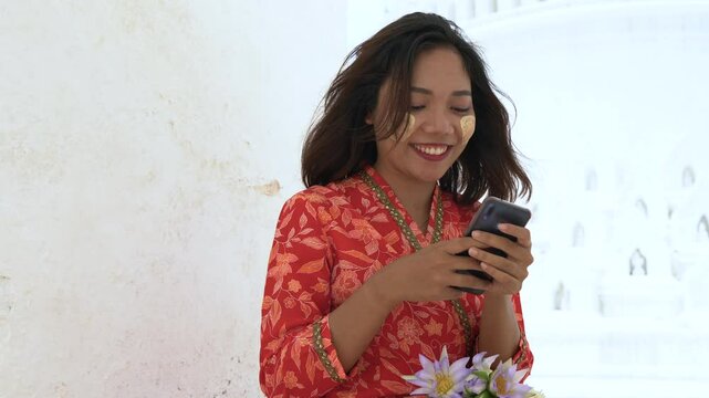Myanmar Woman in traditional Myanmar suit  using mobile and make merit at Hsinbyume Pagoda in Mingun Mandaley, Myanmar.