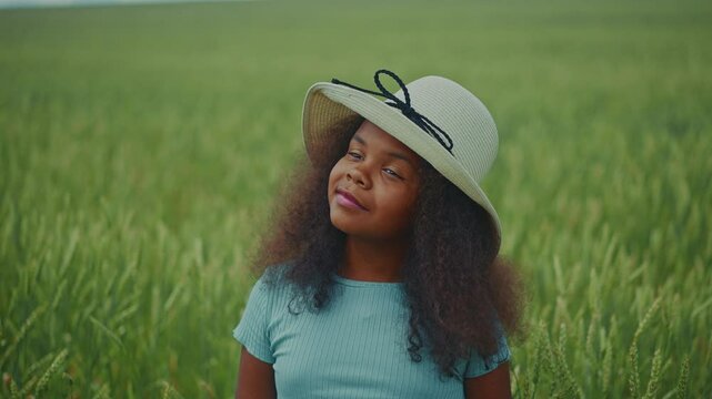Young girl in a sunhat enjoys a peaceful moment in a green field during a summer afternoon