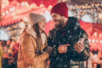 Photo of two people couple students have fun city christmas fair guy point index finger smartphone...