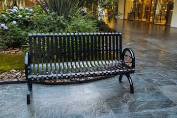 A wrought iron bench is placed in shopping mall for people to sit and rest.