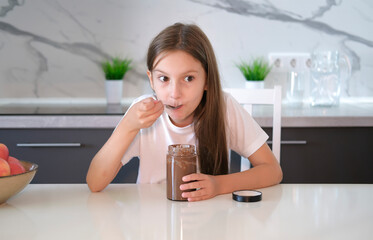 Happy girl having breakfast with chocolate paste at home in modern white kitchen. Baby food concept.