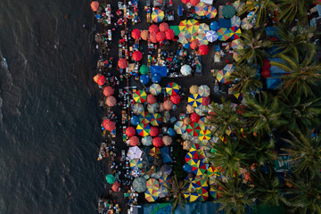 Aerial view of a lively waterfront market filled with colorful umbrellas and crowded stalls,...