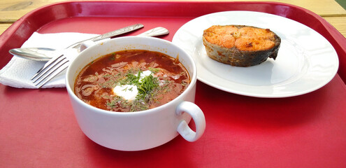Borscht and a piece of fried fish on a red tray.