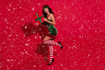 Photo of excited stunning young santa assistant dressed elf holding christmas present smiling isolated red color background