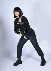 Full length portrait of beautiful black female model with short black hair wearing sci fi futuristic dystopian leather bodysuit costume. Standing pose holding gun weapon, isolated white studio backgro