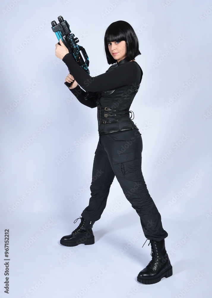 Canvas Prints Full length portrait of beautiful black female model with short black hair wearing sci fi futuristic dystopian leather bodysuit costume. Standing pose holding gun weapon, isolated white studio backgro