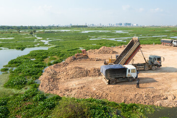 Construction Site with Dump Trucks Unloading Soil Near Green Wetlands
