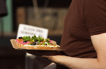 Buying food at farmers market. Midsection body of a man holding paper tray with sandwiches. Low angle of view, profile shot.