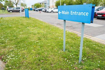 Shallow focus of a generic, blue Main Entrance sign seen at a typical NHS hospital. The sign...