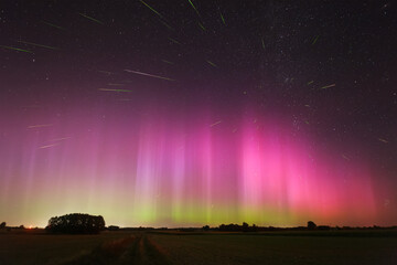 A vibrant display of auroras in a clear night sky over a tranquil rural landscape with a Perseid meteor shower