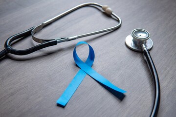 A blue ribbon and a stethoscope placed on a wooden surface. Men's health, prostate cancer awareness...