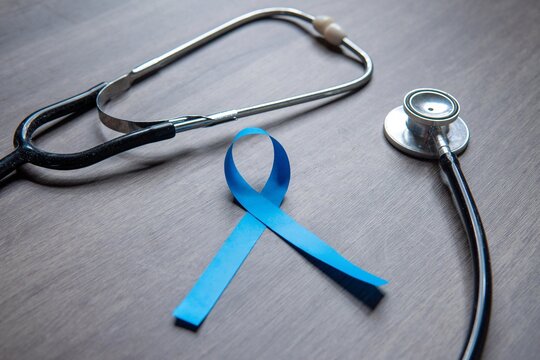 A blue ribbon and a stethoscope placed on a wooden surface. Men's health, prostate cancer awareness concept.