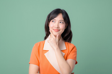 Fototapeta premium Woman in an orange outfit thinking with a thoughtful expression against a green background showing contemplation and curiosity