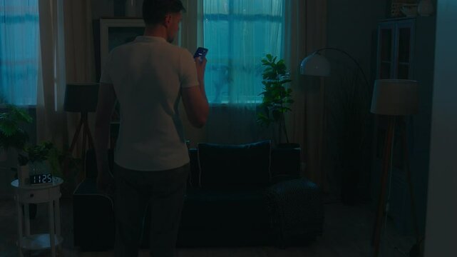 Smart home lighting system man in dark room distant turning lightness electricity modern futuristic house evening night guy male homeowner use mobile phone turn lights on app easy control ai interface
