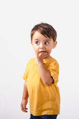 Two-year-old boy covers his mouth with a shy gesture while looking away on white background