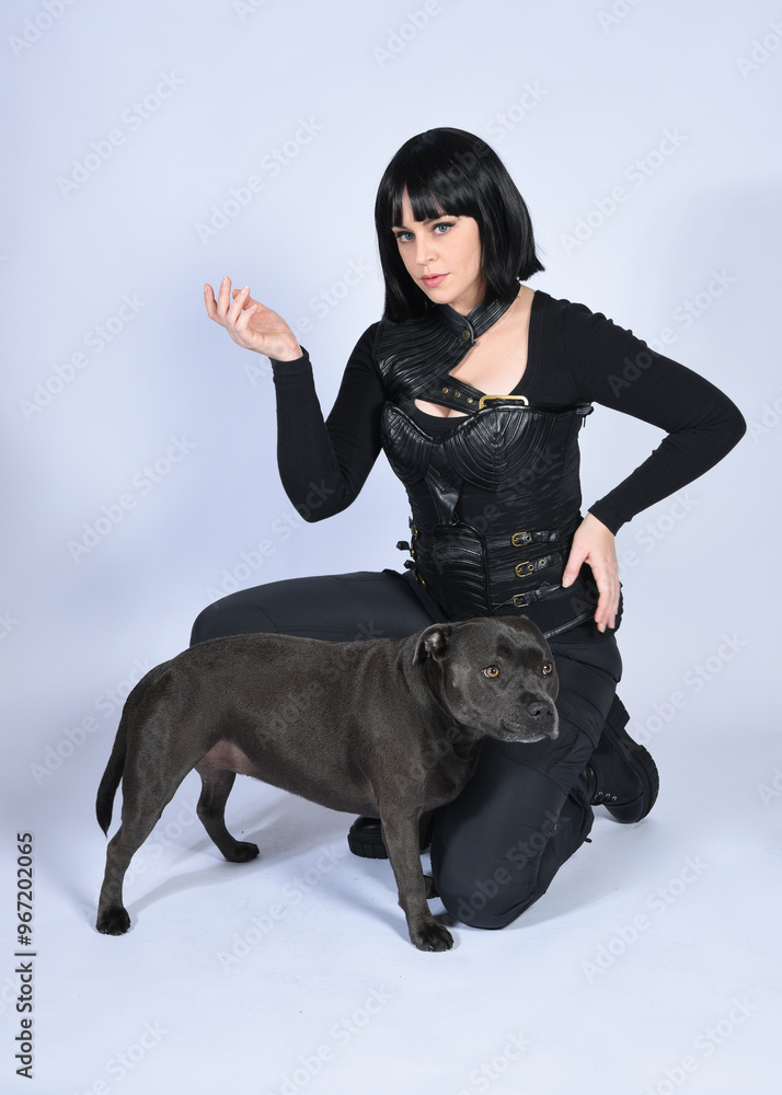 Sticker Full length portrait of beautiful black female model wearing sci fi futuristic dystopian leather bodysuit costume, with animal dog pet companion. sitting pose, isolated white studio background.