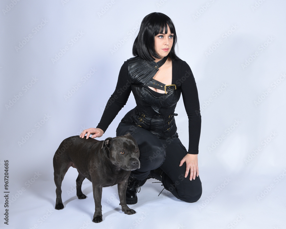 Sticker Full length portrait of beautiful black female model wearing sci fi futuristic dystopian leather bodysuit costume, with animal dog pet companion. sitting pose, isolated white studio background.