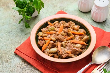 Stew, beef stew with beans and carrots in a ceramic plate on a green concrete background. Beef recipes.
