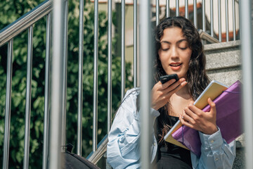 Teenage student sending audio or message with phone on stairs in street