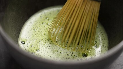 Freshly prepared organic matcha green tea in a bowl with a bamboo whisk. Traditional Japanese drink ceremony. Macro shot