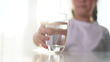 Child drinks water from glass cup on table in the kitchen. small concept of a healthy lifestyle. a girl drinks water in a glass. the girl drinks water and holds a lifestyle glass cup.