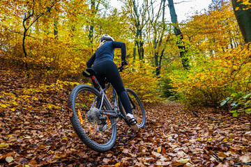 Woman wearing black sporty jacket, black cycling pants and white bike helmet riding her bike uphill...
