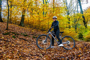 Middle aged woman wearing black sporty jacket, black cycling pants and white bike helmet standing...
