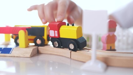 Fototapeta premium Children play with a toy train in kindergarten. Child childhood fun concept. Train with toy is traveling along railway. Children play with toys and trains on the railway in kindergarten lifestyle.