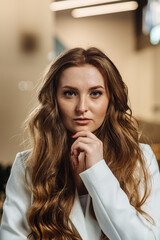 Portrait of confident beautiful girl looking at camera. A woman in a white business suit poses with her chin propped up. Business lady