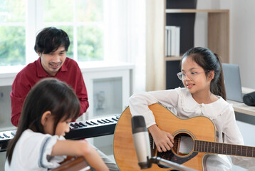 asian female children playing guitar with teacher in the room,adult help kid to learn music,concept of music studying,music education,classical band