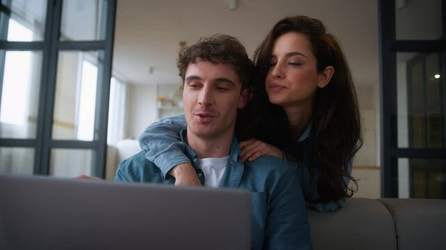Caucasian woman female girl wife girlfriend hugging man back discuss shopping computer talk choose purchase order delivery tickets booking laptop man male guy boyfriend husband couple talking home