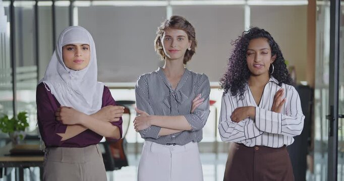 Indian Asian happy young adult gen z proud women lady wear hijab scarf fold hand look cam indoor work place teen mix girls curly hair expert female staff group team cross arms do pose job office day	