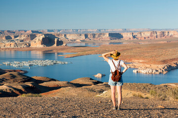 Rear view of woman walking at lakeshore looking at solitary rock formation Lone Rock in Wahweap Bay at Lake Powell, Glen Canyon Recreation Area, Page, Utah, USA