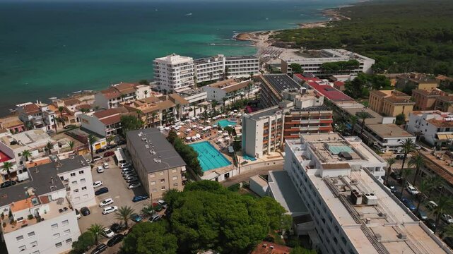 An orbiting drone shot showcasing hotels and pools in Can Picafort, with the stunning sea view in the background.
