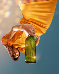 Young beautiful woman in sunny yellow dress holds large green bottle of sparkle wine posing against...